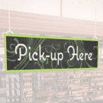 Natural Collection's wayfingding hanging department sign that has "Pick-up Here," digitially printed in white text and on PVC